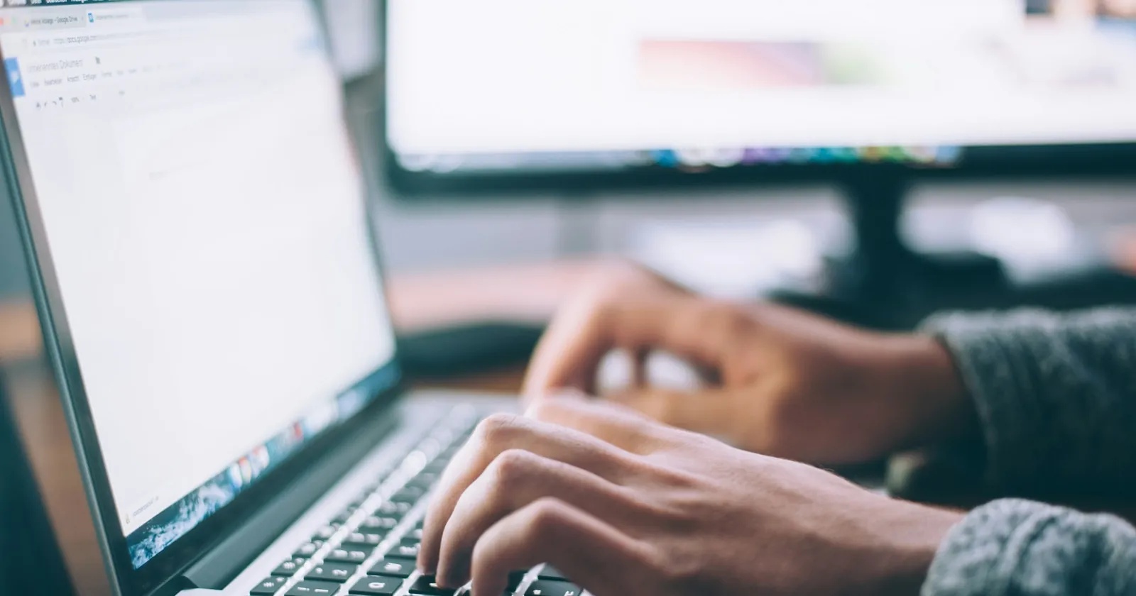 Hands typing on a laptop keyboard at a desk