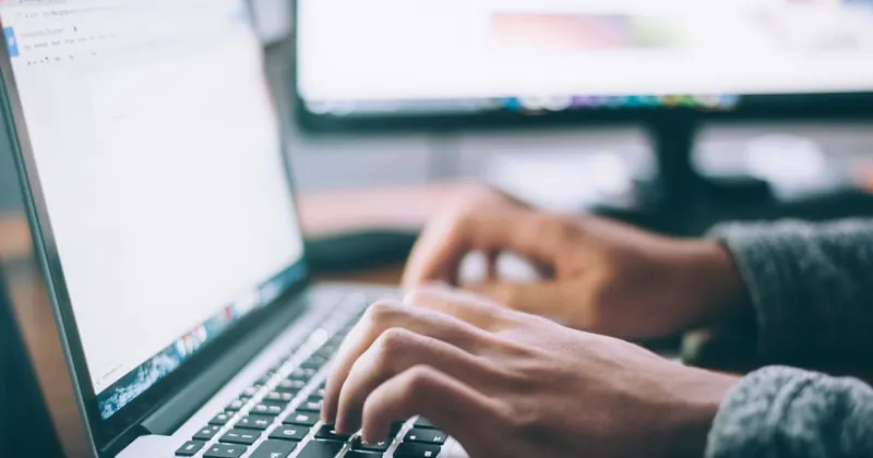 Hands typing on a laptop keyboard at a desk